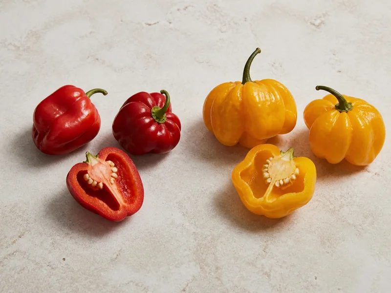 Whole and cut Aji Dulce and Scotch Bonnet peppers arranged at equal scale for identification