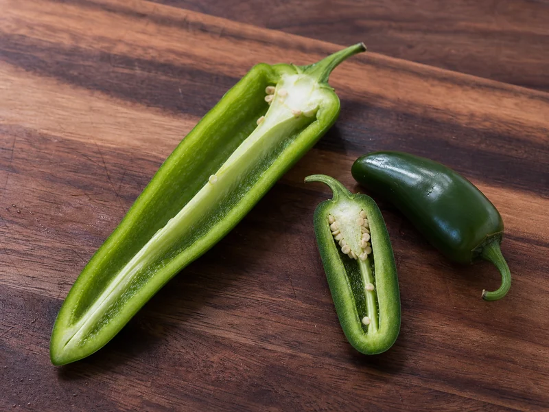 Long Anaheim pepper beside shorter thick-walled Jalapeños on a cutting board