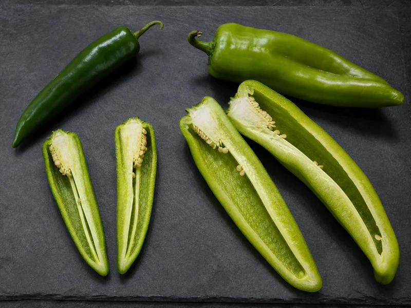 Whole and cut Anaheim and NuMex Big Jim green chiles showing differences in pod width and cavity size