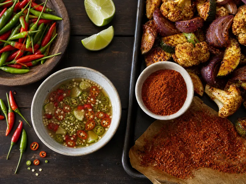 Fresh bird's eye chiles and Thai-style dipping sauce beside cayenne powder and roasted vegetables