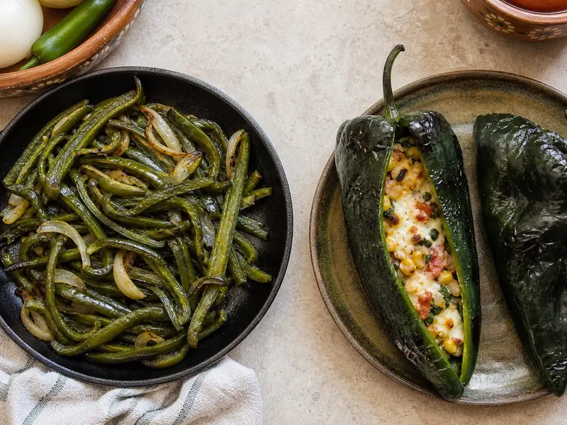 Roasted chilaca strips beside a broad poblano pepper prepared for stuffing