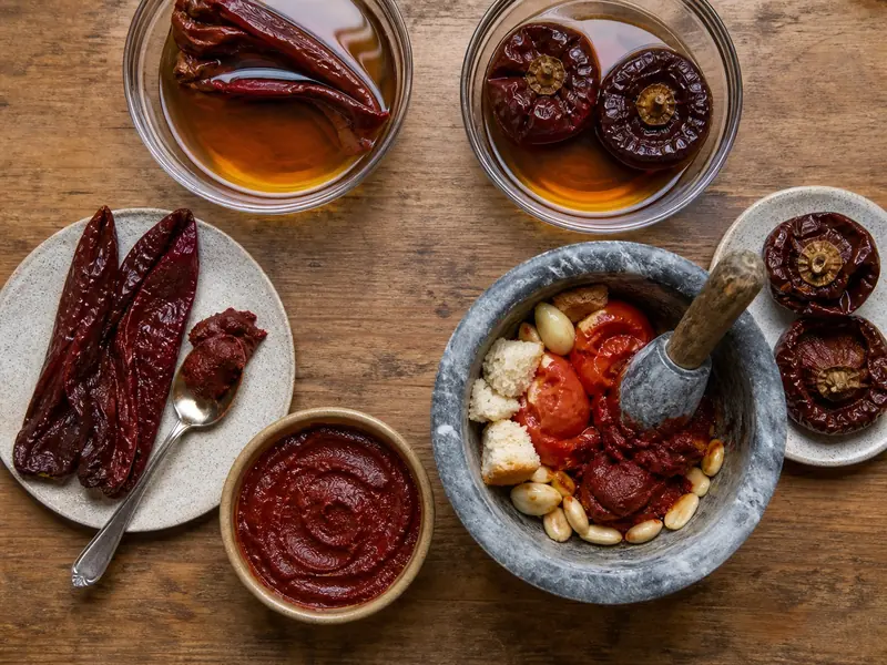 Rehydrated long Choricero peppers scraped into red pulp beside round Nora peppers and a romesco-style base