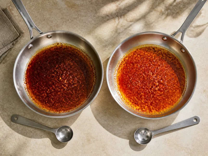 Equal measures of dark and light chili powder blooming in separate skillets of oil