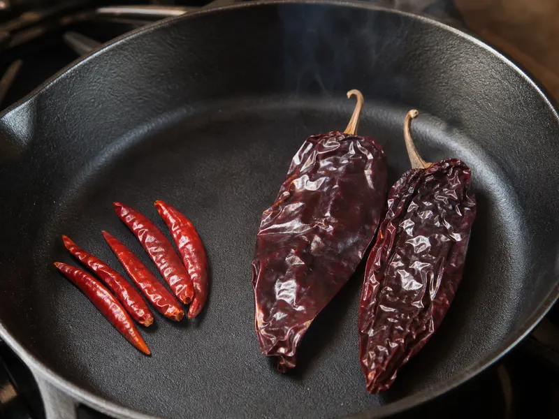 Chile de arbol and guajillo pods toasting in a dry cast-iron skillet