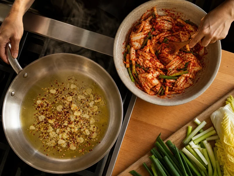 Crushed red pepper blooming in garlic oil beside cabbage coated with gochugaru paste