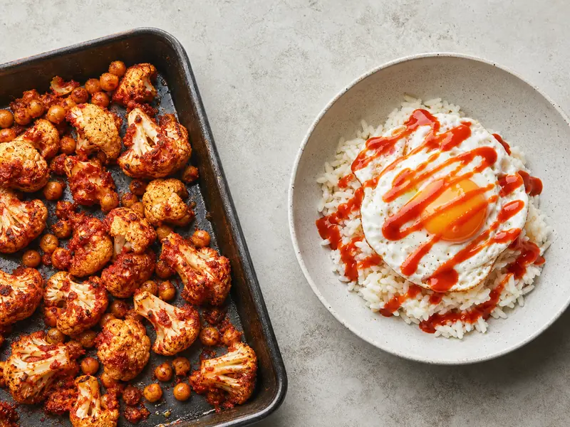 Harissa coating roasted vegetables beside sriracha drizzled over a finished bowl