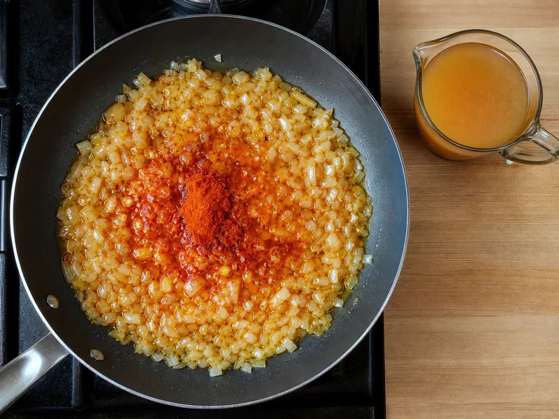 Paprika blooming gently in oil beside a pan with liquid ready to stop scorching