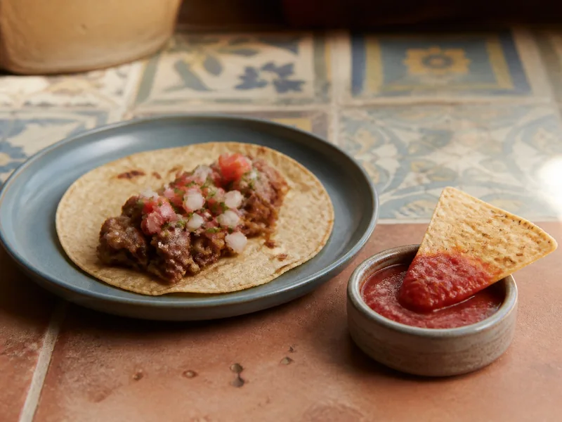 Pico de gallo topping a taco beside a tortilla chip coated with red salsa