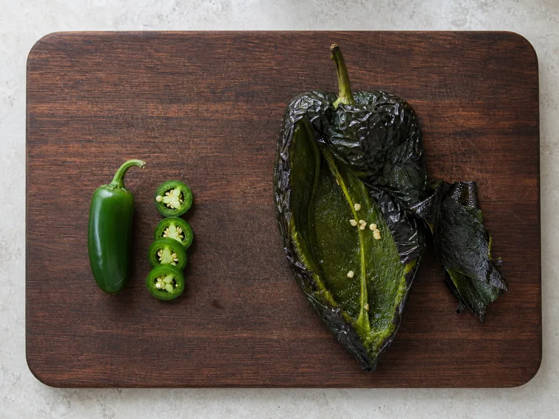Sliced green jalapeño beside a roasted and peeled poblano pepper