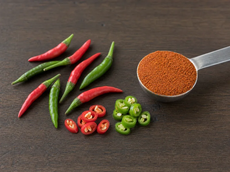 Sliced red and green Thai bird chiles beside a measured spoon of cayenne powder