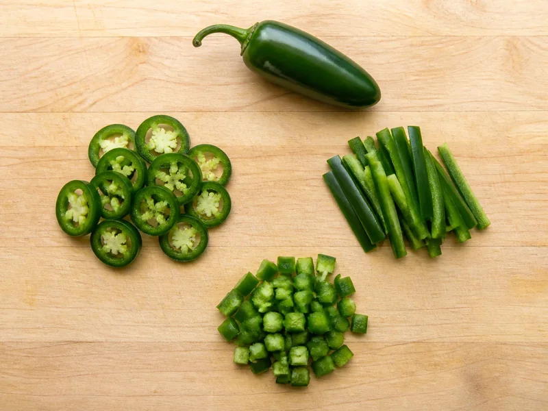 Jalapeno rings, strips, and dice arranged separately on a maple cutting board