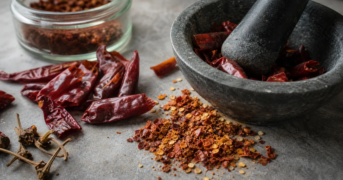 Coarse homemade red pepper flakes being crushed from dried chiles with a mortar and pestle