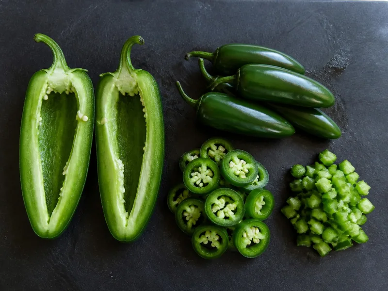 Large halved stuffing jalapeno beside smaller whole, sliced, and diced jalapenos