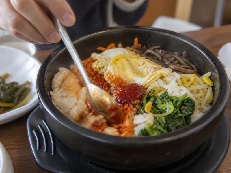 Gochujang being mixed through rice and vegetables in bibimbap