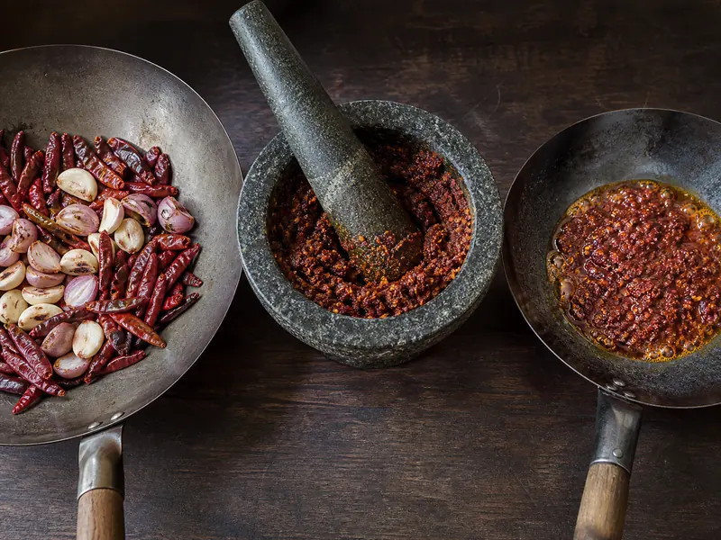 Dried chiles, shallots, and garlic shown roasted, ground in a mortar, and fried in oil