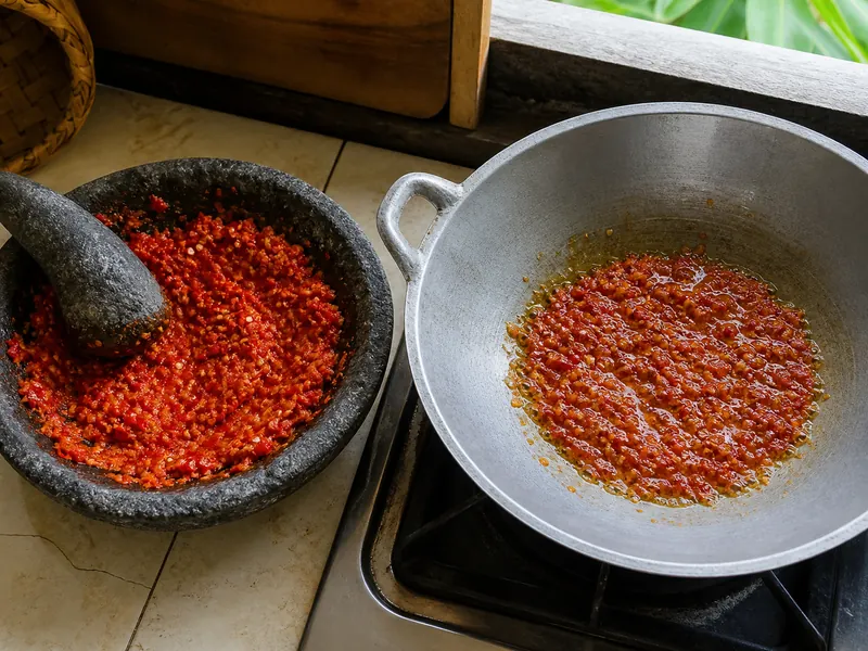 Fresh coarse sambal oelek in a mortar beside the same paste gently cooking in a wok
