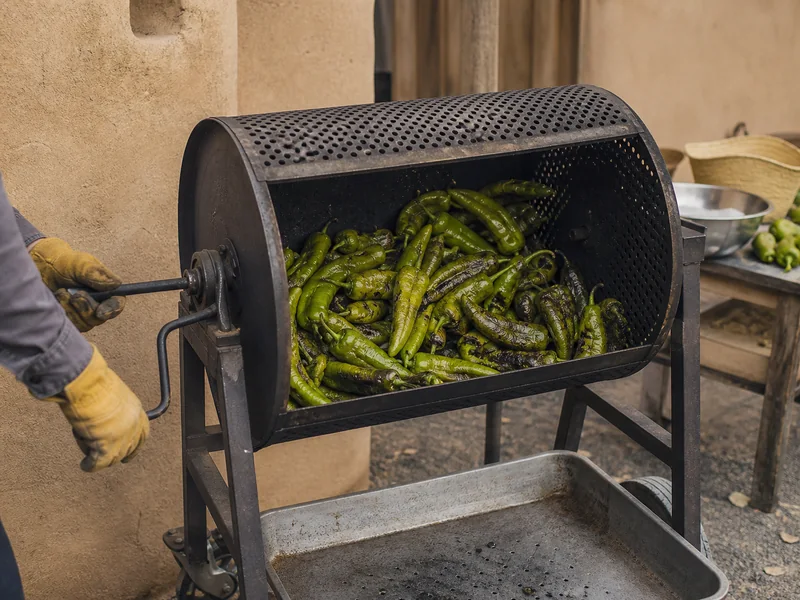 Green New Mexican chile pods roasting over a perforated metal drum