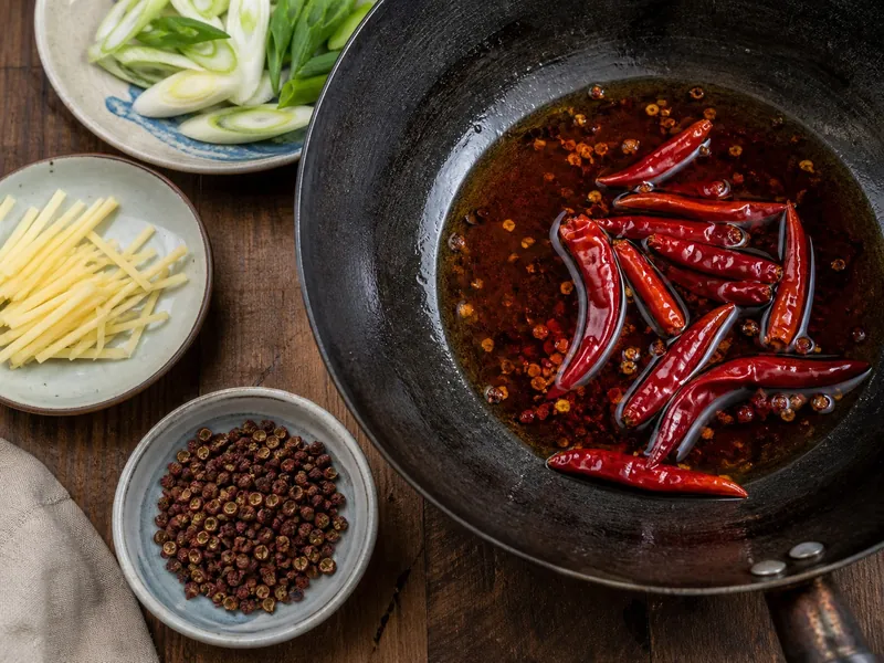 Dried Chinese chiles blooming in oil with Sichuan pepper husks kept in a separate bowl