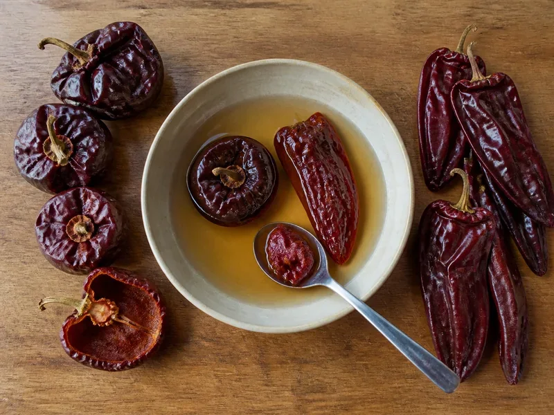 Round ñora and long choricero peppers before and after soaking