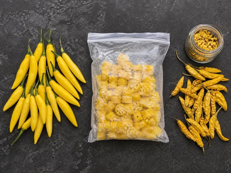Fresh yellow Aji Pineapple peppers beside frozen pieces, dried pods, and coarse flakes