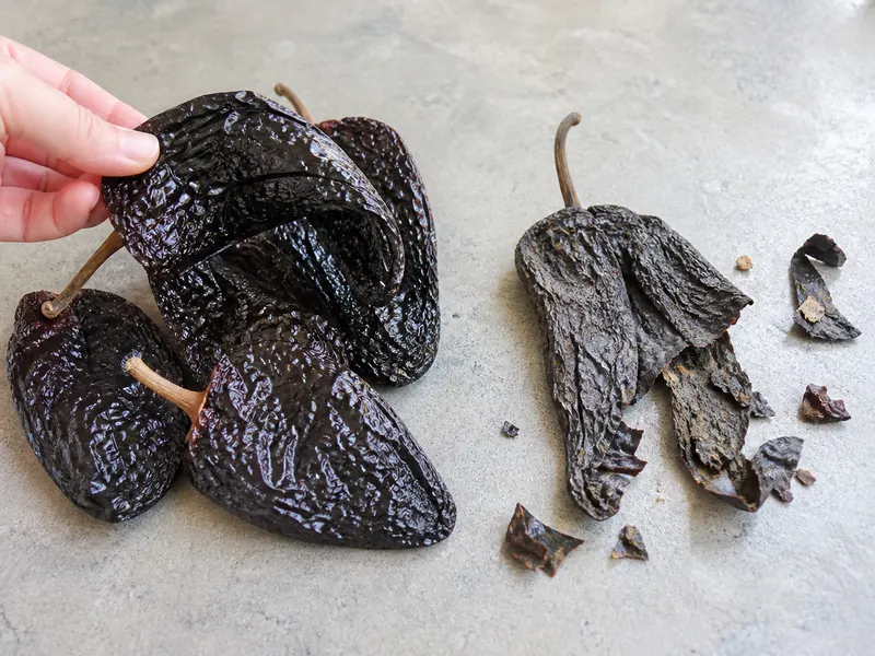 Pliable glossy ancho pods beside a faded brittle pod with broken pieces