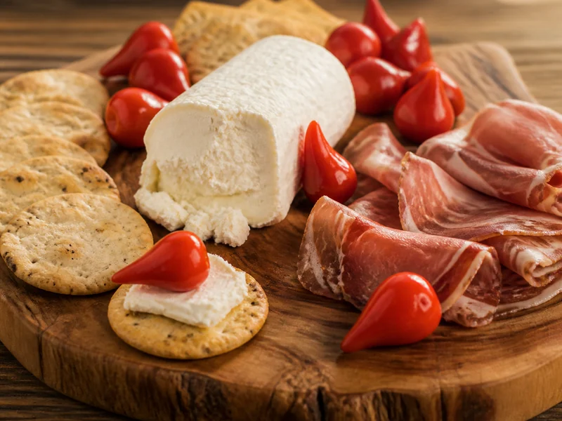 Biquinho peppers on a cheese board, drained and scattered over soft cheese and crackers