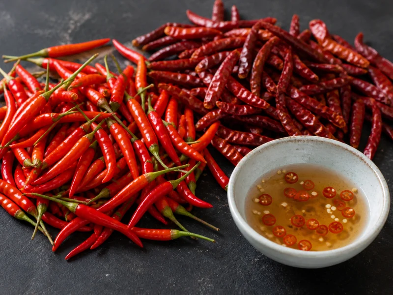 Dried and fresh bird's eye chilies beside a bowl of Thai dipping sauce