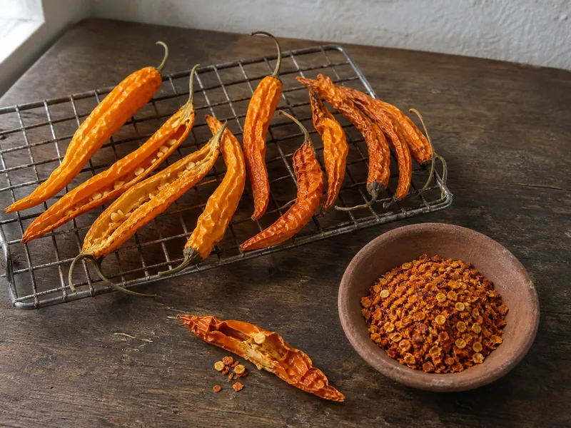 Golden Criolla Sella pods drying on a rack beside coarse pepper flakes
