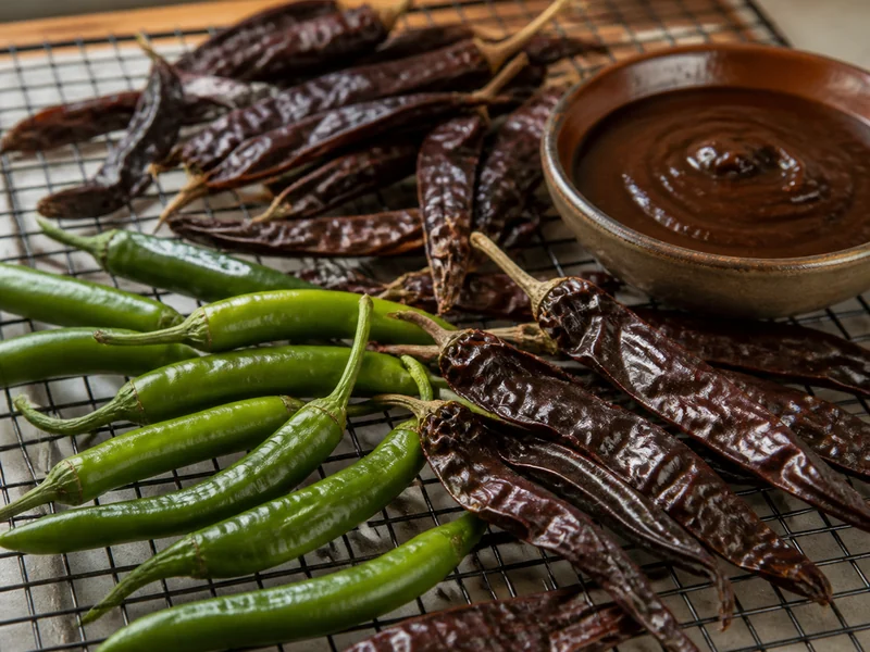 Long tapering Holy Mole pods drying, beside a bowl of dark mole sauce