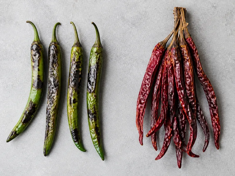 Blistered roasted green New Mexico chile beside dried red pods tied into a ristra