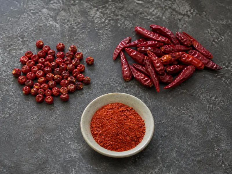 Whole round chiltepin beside elongated piquin and ground cayenne on a stone work surface